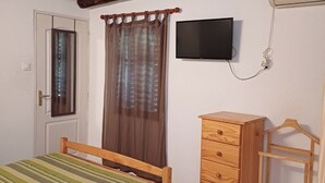 Ein Schlafzimmer mit Bett, Holzkommode, Fernseher und einer Tür.