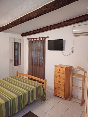 A bedroom with a bed, wooden dresser, TV, and a door.