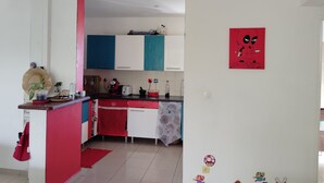 Una cucina con mobili bianchi, un piano di lavoro rosso e una parete rossa. Si notano diversi elettrodomestici da cucina e una pianta in vaso sul piano.
