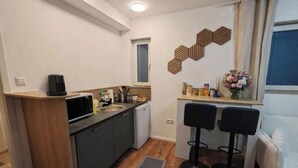 Cocina compacta con microondas, pileta y heladera pequeña. Hay dos taburetes negros y un sofá blanco.