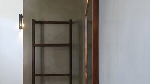 Een kamer met een houten ladder die tegen een muur staat, een spiegel met metalen frame en een wandlamp.