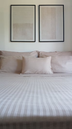 A bed with striped bedding, two framed abstract artworks on the wall, and a sofa with matching cushions.