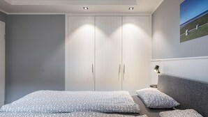 Un dormitorio con cama, almohadas, mesita de noche, lámpara y armario.