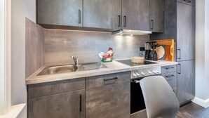Una cocina compacta con gabinetes oscuros, un lavamanos de acero inoxidable, una estufa y una sola silla.