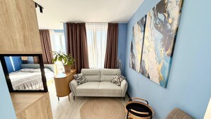 A modern living room with a sofa, a TV, a plant, and a wall art piece. - Cozy Sea Style Studio with Balcony (Sunny Beach)