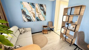 A living room with a sofa, a coffee table, a bookshelf, a chair, and a large abstract painting on the wall. - Cozy Sea Style Studio with Balcony (Sunny Beach)