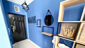 A hallway with a black door, a wall-mounted light fixture, a hanging mirror, and shelves with various items. - Cozy Sea Style Studio with Balcony (Sunny Beach)
