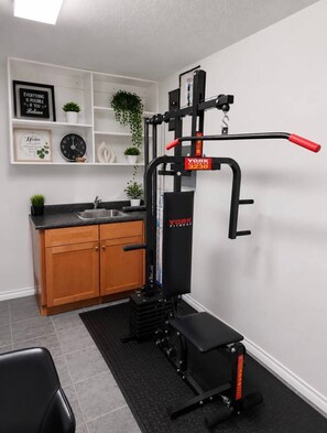 Ein Heimfitnessraum mit einer Klimmzugstange, einer Bank und einem an der Wand befestigten Trainingsgerät.
