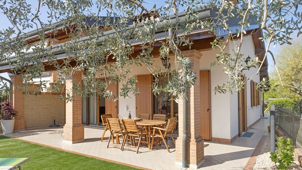 Un patio techado con mobiliario exterior, un muro de ladrillo y un césped bien cuidado.