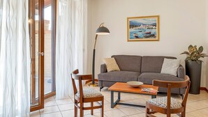 Una sala de estar con un sofá, dos sillones, una mesa de centro, una lámpara de pie, un cuadro y una planta en maceta.