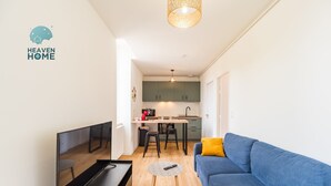 Ein modernes Wohnzimmer mit Fernseher, Sofa und Couchtisch, das in eine Küche mit Essbereich übergeht.