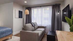 Une chambre d’hôtel moderne équipée d’un canapé, d’un lit, d’une télévision et d’une grande fenêtre avec des rideaux.