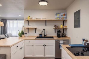 A compact kitchen with a sink, cabinets, and a countertop. There are shelves above the sink holding dishes and a coffee maker. - Stylish Downtown Studio - Free Parking plus Kitchen (Anchorage)