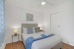 A bedroom with a bed, bedside tables, a ceiling fan, and a wall-mounted artwork.