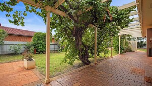 A covered patio area with a brick floor, a pergola structure, and a large tree. - Sunrise on Sovereign - Retro Family Entertainer (Dubbo)