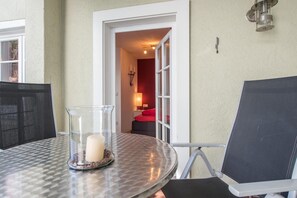 Et rundt glastop med et lys og dekorative sten, en sort stol, og en døråbning ind til et rum med et rødt sengetæppe.