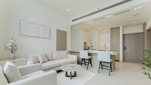 A modern living room with a sofa, coffee table, and a kitchen area with a bar and chairs. - PVH - Lavish 1BR - Private Pool (Dubai)