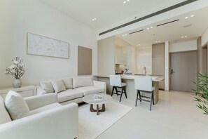 A modern living room with a sofa, coffee table, and a kitchen area with a bar and chairs. - PVH - Lavish 1BR - Private Pool (Dubai)