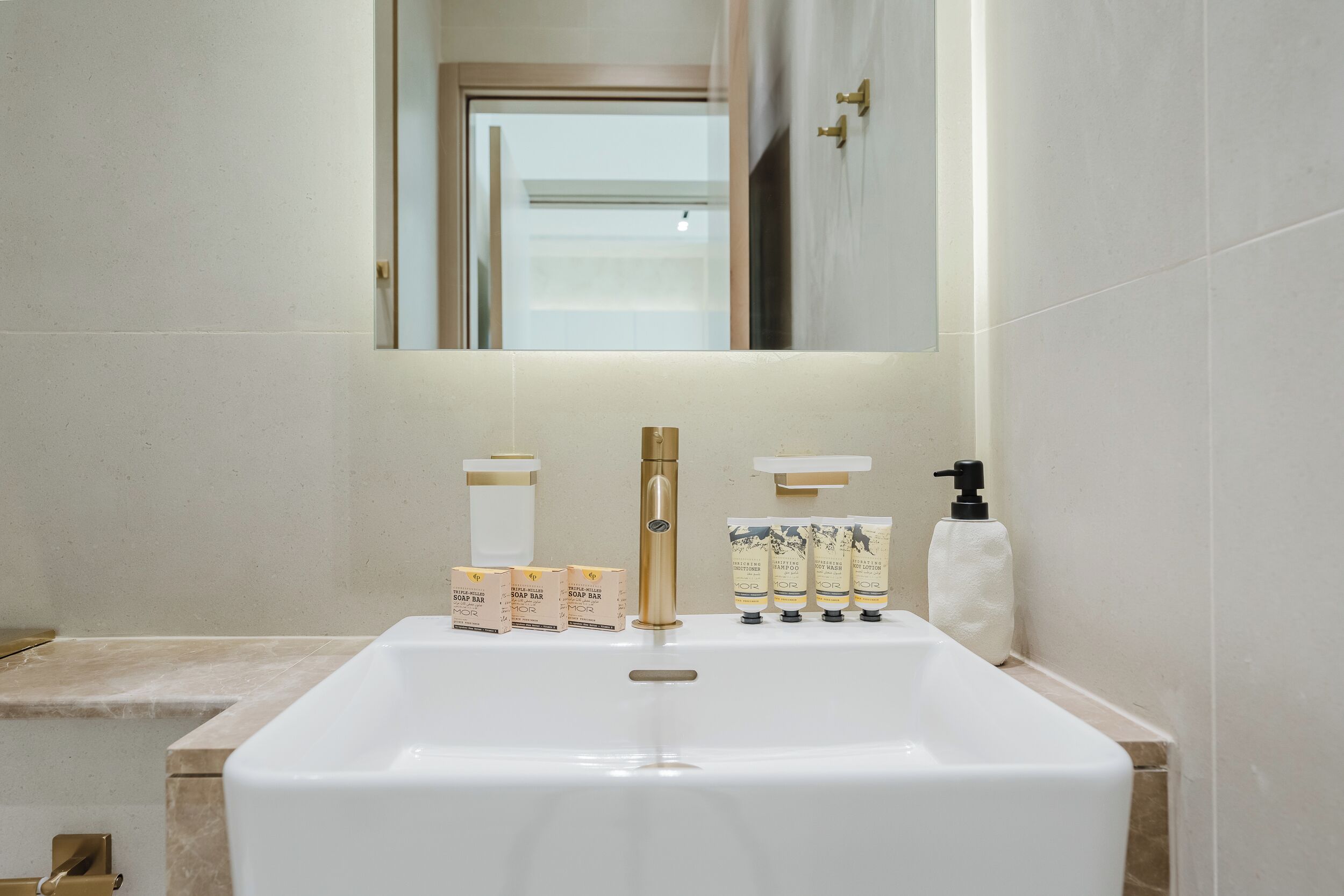 Un baño con lavamanos blanco, grifo dorado y dispensadores de jabón.
