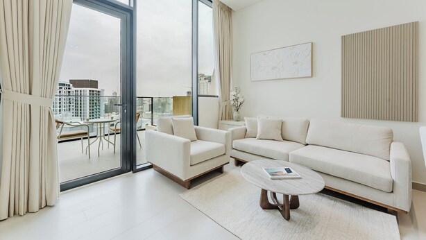 A modern living room with a sofa, armchair, and coffee table, large windows with curtains, and artwork on the walls. - PVH - Lavish 1BR - Private Pool (Dubai)