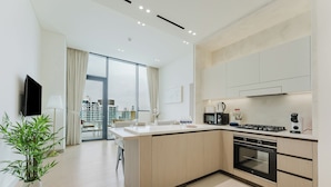 A modern kitchen with a central island, built-in oven, and a dining area with a view of the city. - PVH - Lavish 1BR - Private Pool (Dubai)