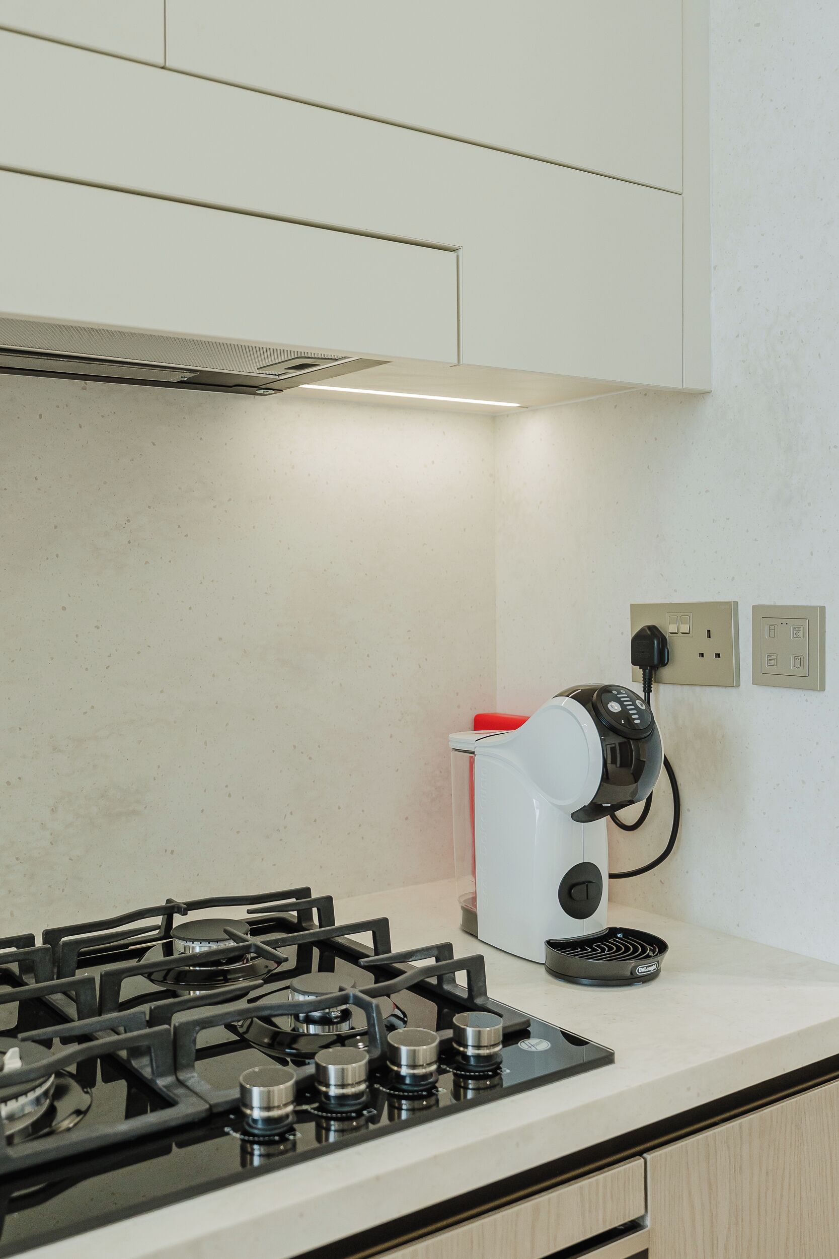 Una cocina con estufa a gas, cafetera y toma de corriente.