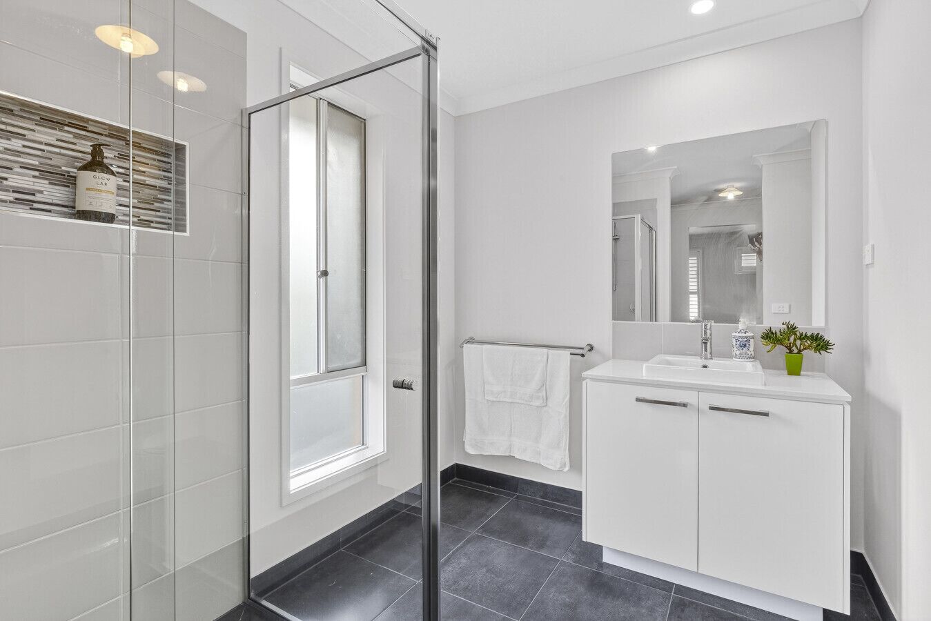 Un bagno moderno con box doccia in vetro, mobili bianchi e uno specchio sopra il lavandino.
