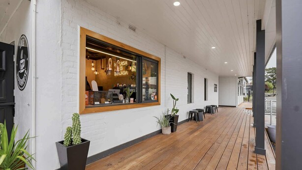 Cafè amb terrassa de fusta, parets de maó blanc i plantes en testos.