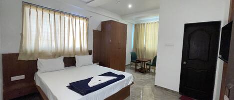 A hotel room with a bed, a wardrobe, a desk with a chair, a ceiling fan, and a door.