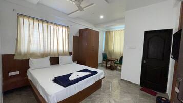 Habitación de hotel con cama, armario, escritorio, silla, cortinas y puerta.