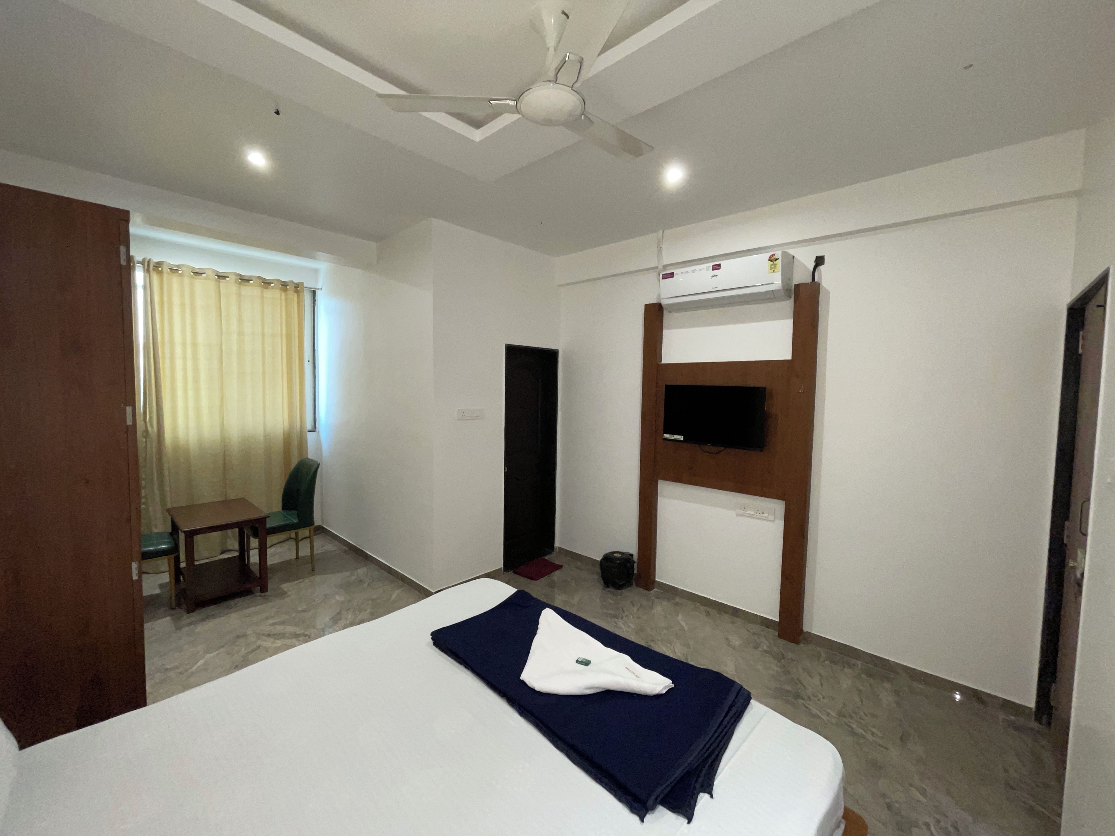 Ein Hotelzimmer mit einem Bett, einem Schreibtisch, einem Stuhl, einem an einer Holzplatte befestigten Fernseher und einer Klimaanlage.