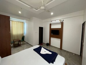 A hotel room with a bed, a desk, a chair, a television, and an air conditioning unit. - Atithi Executive Lodging (Pune)