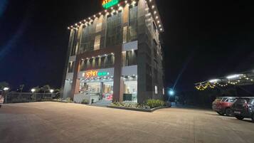 Un bâtiment portant l’enseigne « ATHITHI EXECUTIVE ROOMS », une devanture de magasin avec l’enseigne « BHUTNEDHAR » et un espace de stationnement où se trouvent plusieurs véhicules.