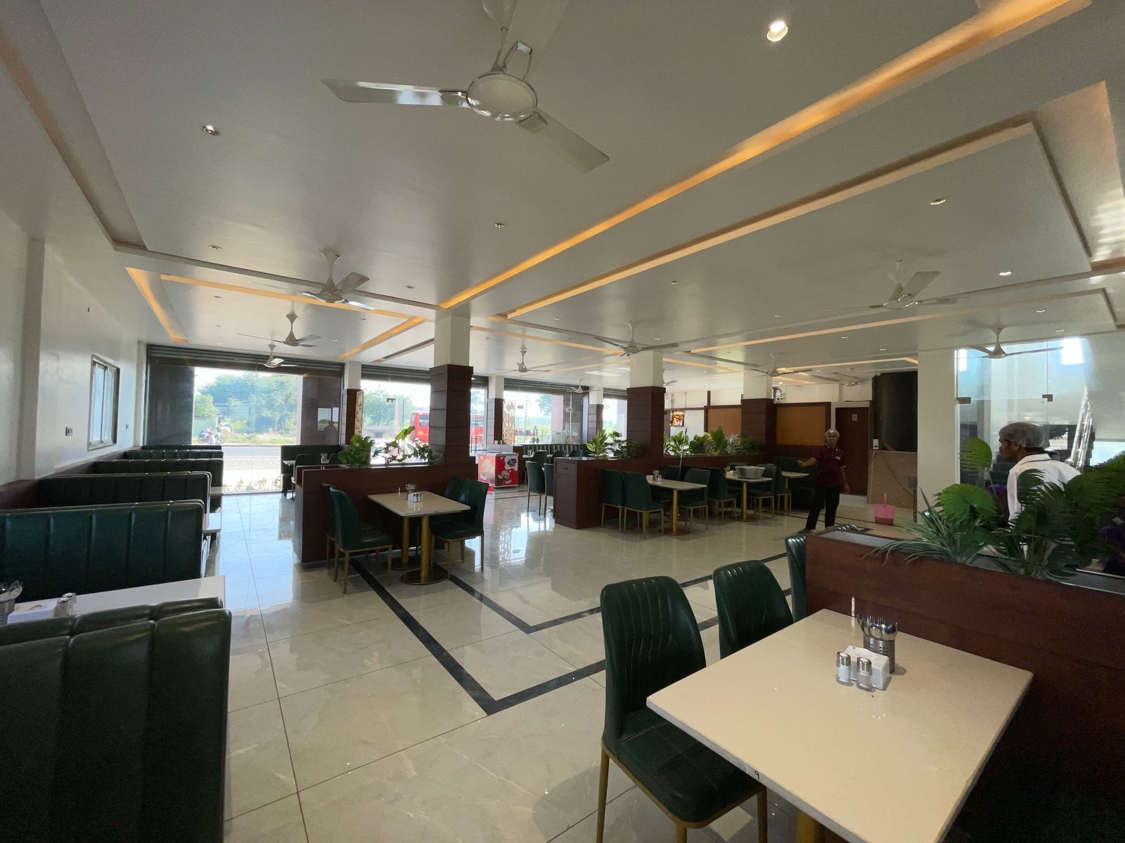 Ein geräumiges Restaurant mit hohen Decken, mehreren Sitzbereichen inklusive Sitzecken und Tischen sowie Deckenventilatoren.