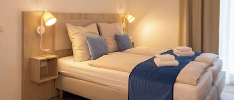 Un lit bien fait, avec des oreillers, une table de chevet et des lampes de lecture fixées au mur.