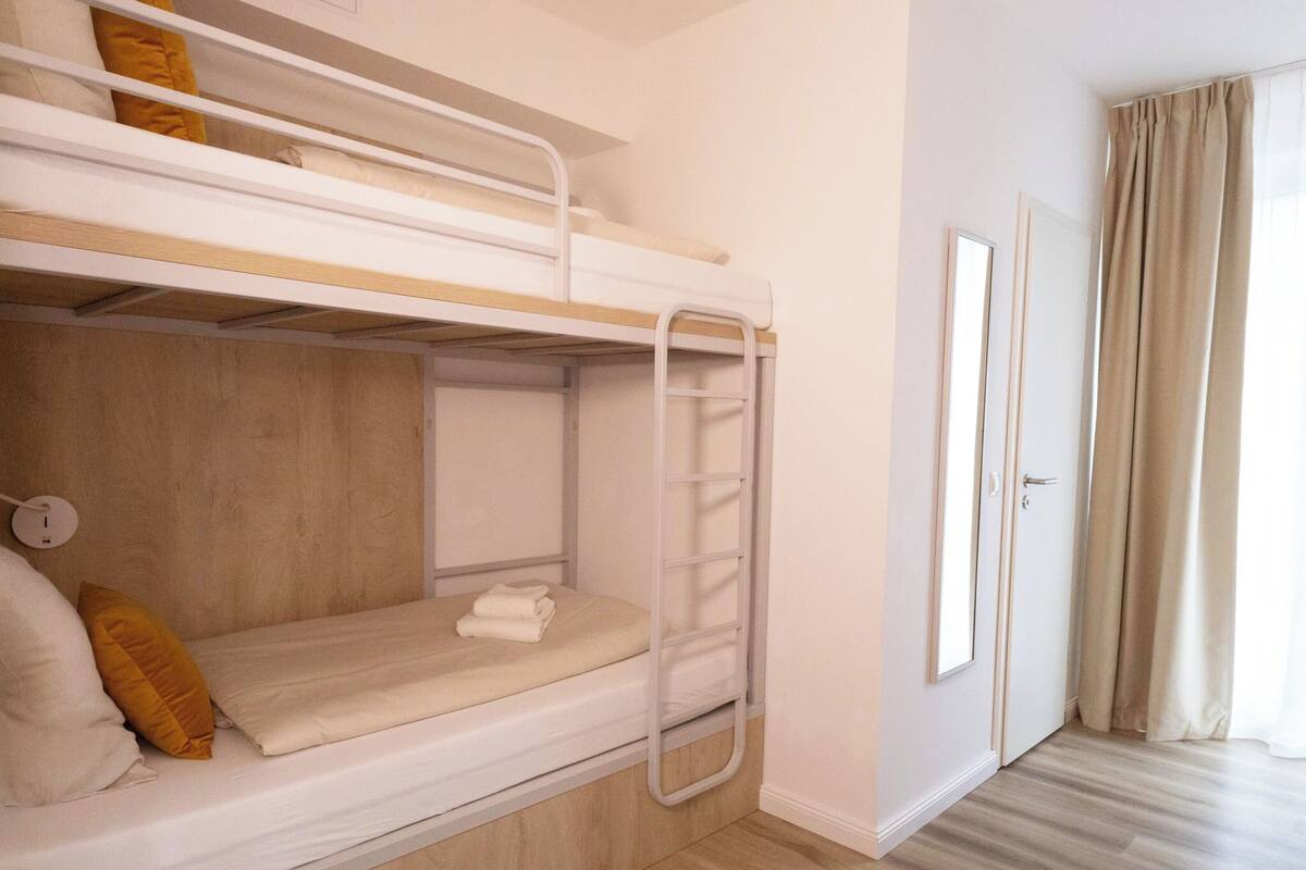 A bunk bed room with a wooden floor, a door, and a window with curtains.