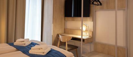 A hotel room with a bed, a desk with a chair, a TV, and a wardrobe.