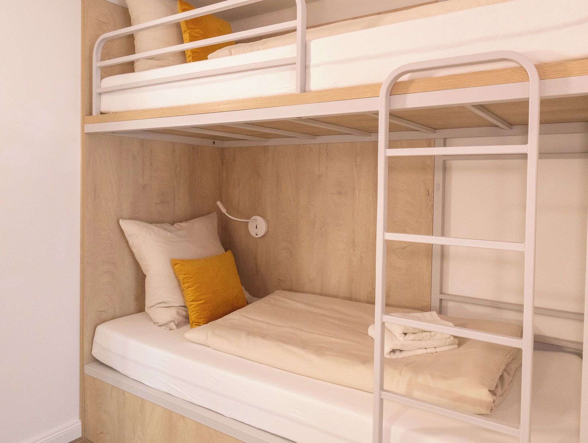 Een slaapkamer met een stapelbed, een houten hoofdbord, een witte muur en een witte nachtkastje met een lamp.