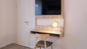 Ein Zimmer mit Schreibtisch, Stuhl, Fernseher und Lampe.