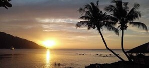 A sunset over a beach with palm trees and a distant mountain. - Manzil Anilao Unit 1 - Ground Floor 1st Room (Mabini)