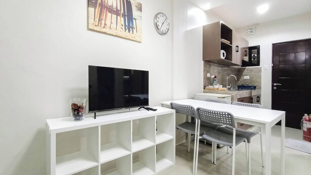 A modern kitchen with a flat-screen TV, dining table, chairs, and a clock on the wall. - Manzil Anilao Unit 1 - Ground Floor 1st Room (Mabini)