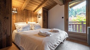 Ein Schlafzimmer mit Holzwänden, einem Bett, Kissen und einem Fenster mit Blick auf Grünflächen.