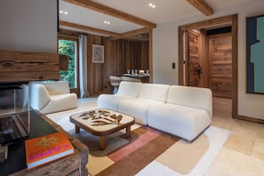 A modern living room with a white sofa, a coffee table, and a TV. There is a wooden ceiling and a door leading to another room. - Superb Chalet Isatis, Renovated in Megeve (Megeve)