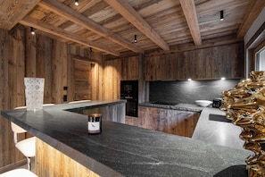 A modern kitchen with wooden walls, a black countertop, and a unique golden sculpture. - Superb Chalet Isatis, Renovated in Megeve (Megeve)