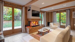 Ein modernes Wohnzimmer mit Kamin, großen Fenstern und einer Couch.
