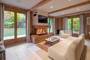 A modern living room with a fireplace, large windows, and a sofa. - Superb Chalet Isatis, Renovated in Megeve (Megeve)
