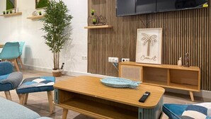 Een moderne woonkamer met een houten tv-meubel, een grote televisie en een gezellige zithoek met blauwe stoelen en een houten tafel.