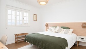 A bedroom with a bed, bedside tables, a chair, a window, and a hanging light fixture. - Vivelorural Casa Marao Great sea Views (Arucas)