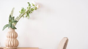 A beige vase with a plant on a wooden table against a plain wall. - Vivelorural Casa Marao Great sea Views (Arucas)