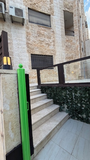 Un edificio de piedra con una escalera que lleva a un balcón, unidades de aire acondicionado y una barandilla metálica.